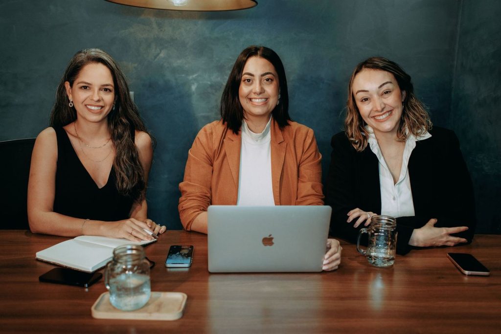 Three women smiling around a table with laptops