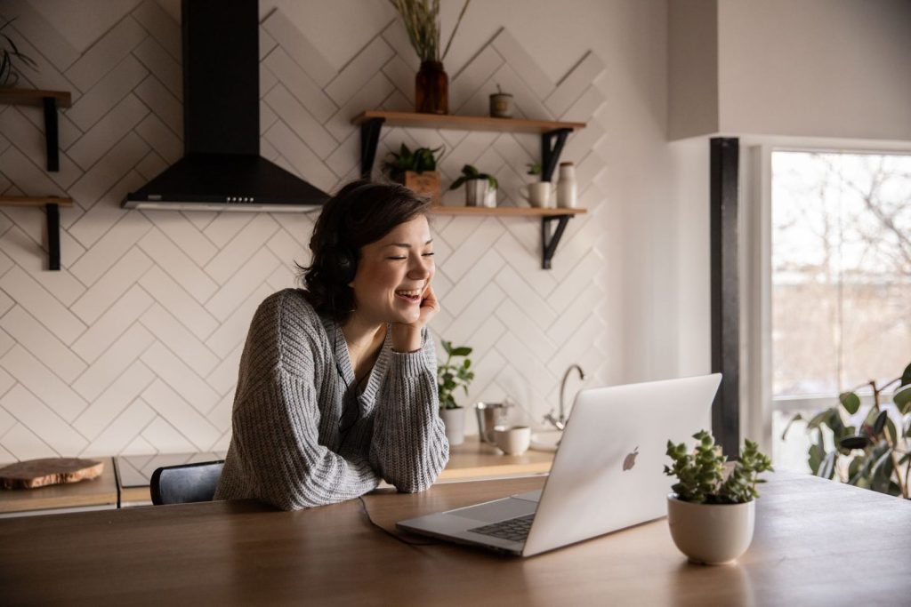 A smiling woman on a video call at her kitchen table